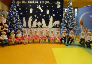 Grupa dzieci recytuje wiersz, w tle dekoracja świąteczna.